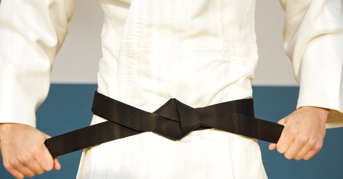 A close-up view of a martial artist tightening a perfectly knotted black belt over a white gi, illustrating the culmination of achievement when studying karate belt levels explained.