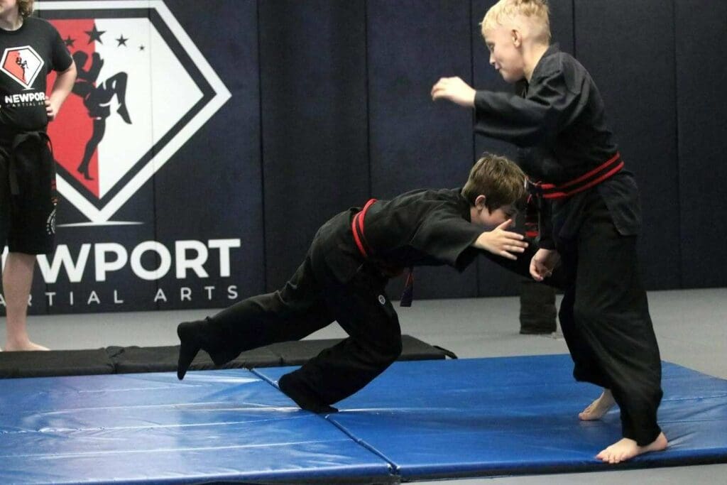 Two young students practicing a takedown entry on the mat during a self-defense class, what you learn in self defense lessons